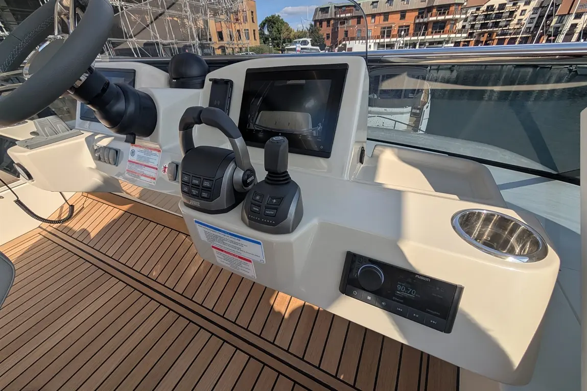 Boat control panel featuring a steering wheel, touchscreen, controls, and a Fusion audio system on a wooden deck.